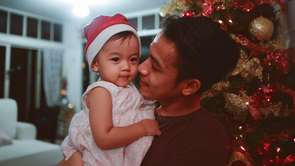 A man holding a smiling baby girl with a Christmas tree in the background